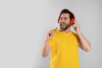 Photo of Emotional man singing while listening music with headphones on light grey background. Space for text