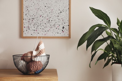 Photo of Yarn balls and knitting needles in metal basket on wooden table indoors, space for text. Creative hobby