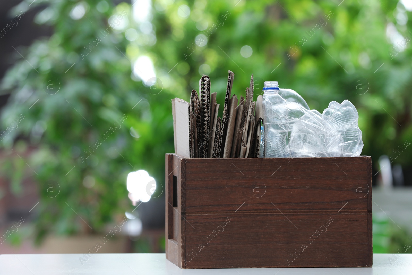 Photo of Wooden crate with different garbage on blurred background, space for text. Waste recycling concept