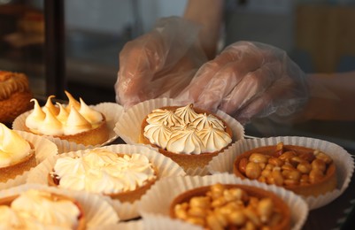 Photo of Seller taking tasty tartlet from showcase in bakery shop, closeup