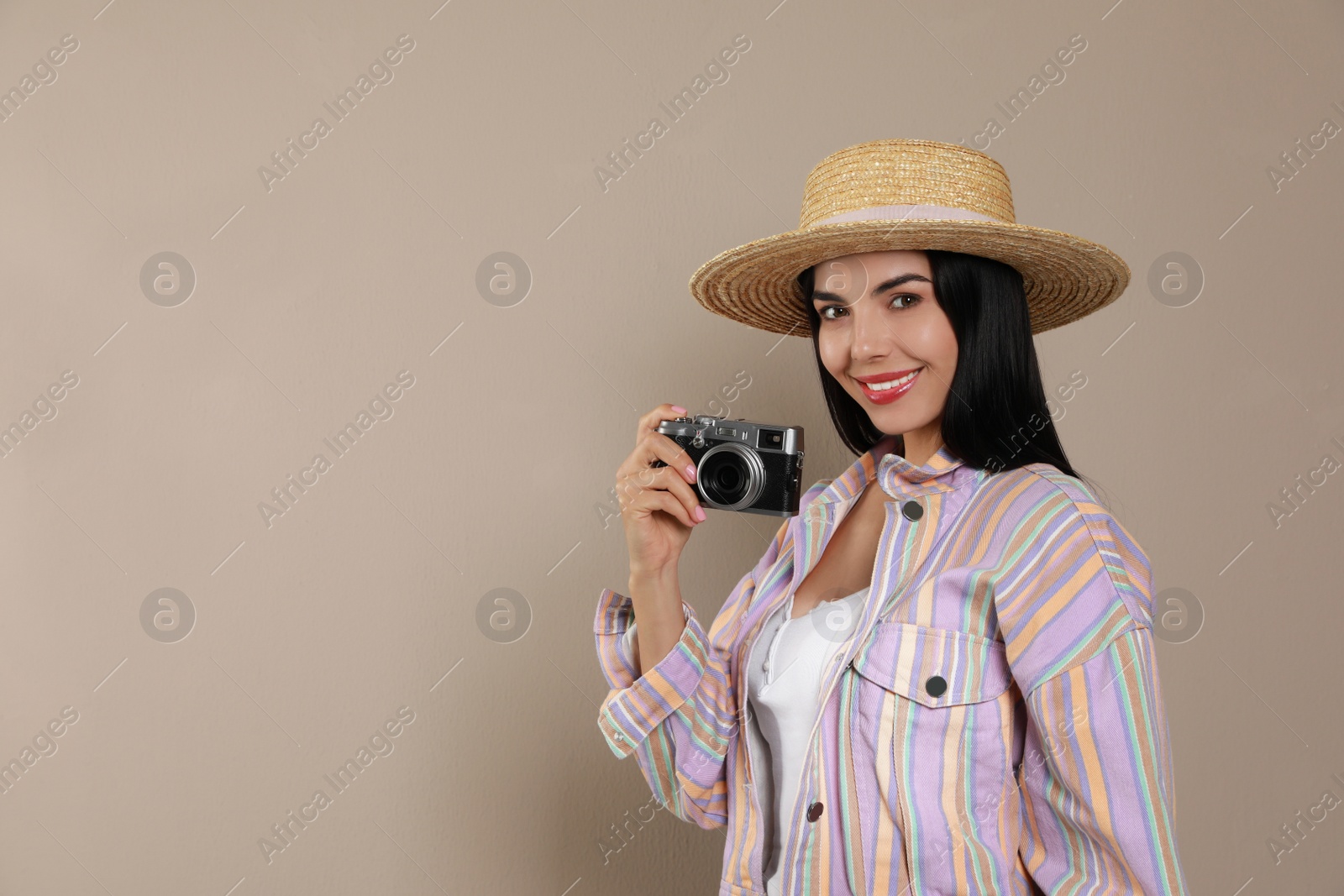 Photo of Beautiful young woman with straw hat and camera on beige background. Space for text