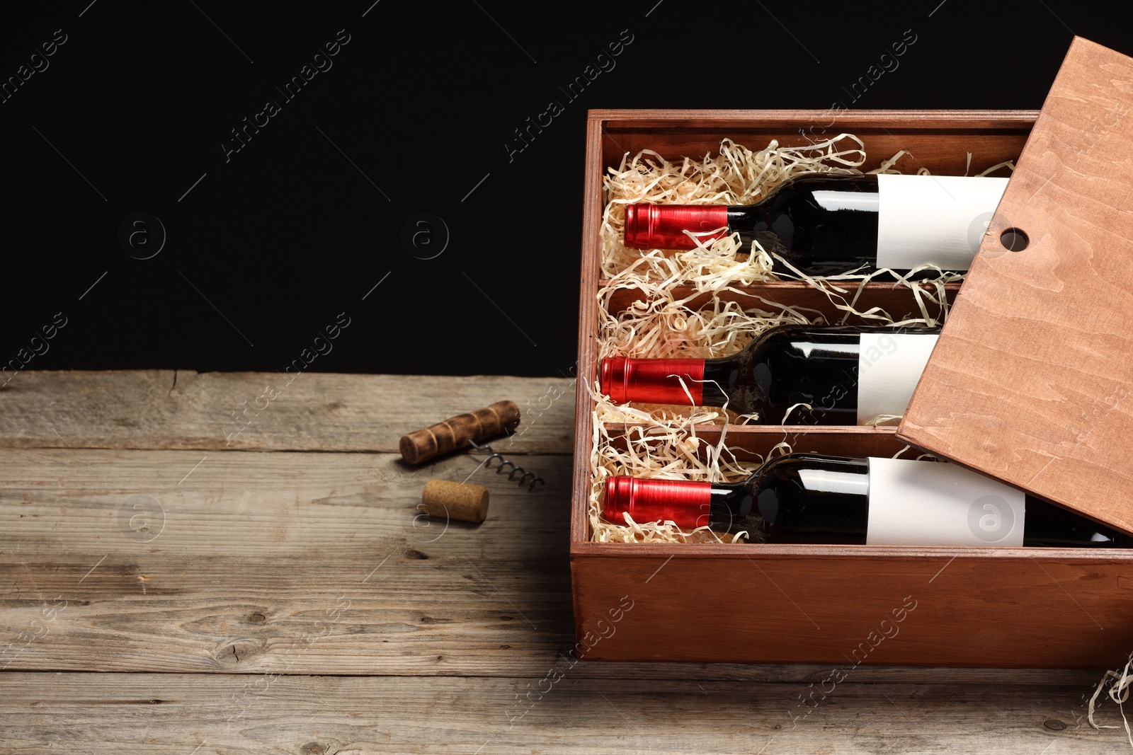 Photo of Box with wine bottles on wooden table against black background. Space for text