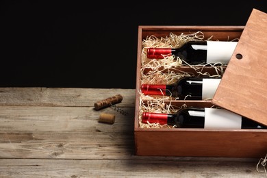 Photo of Box with wine bottles on wooden table against black background. Space for text