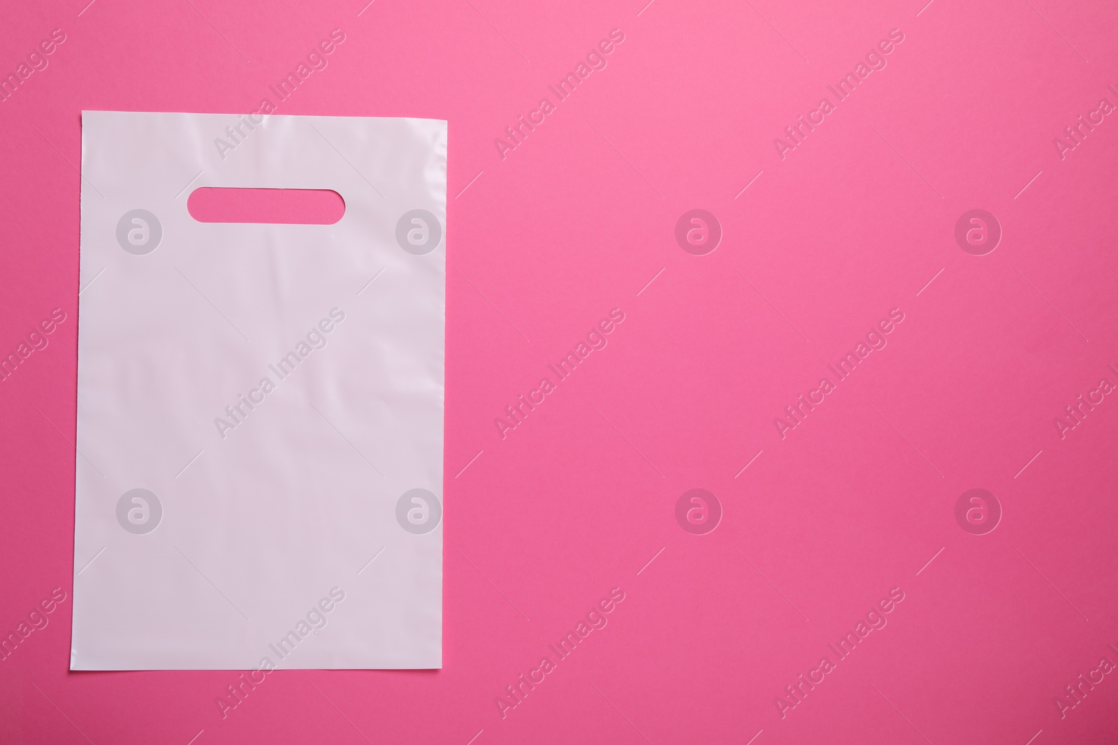Photo of White plastic bag on bright pink background, top view. Space for text