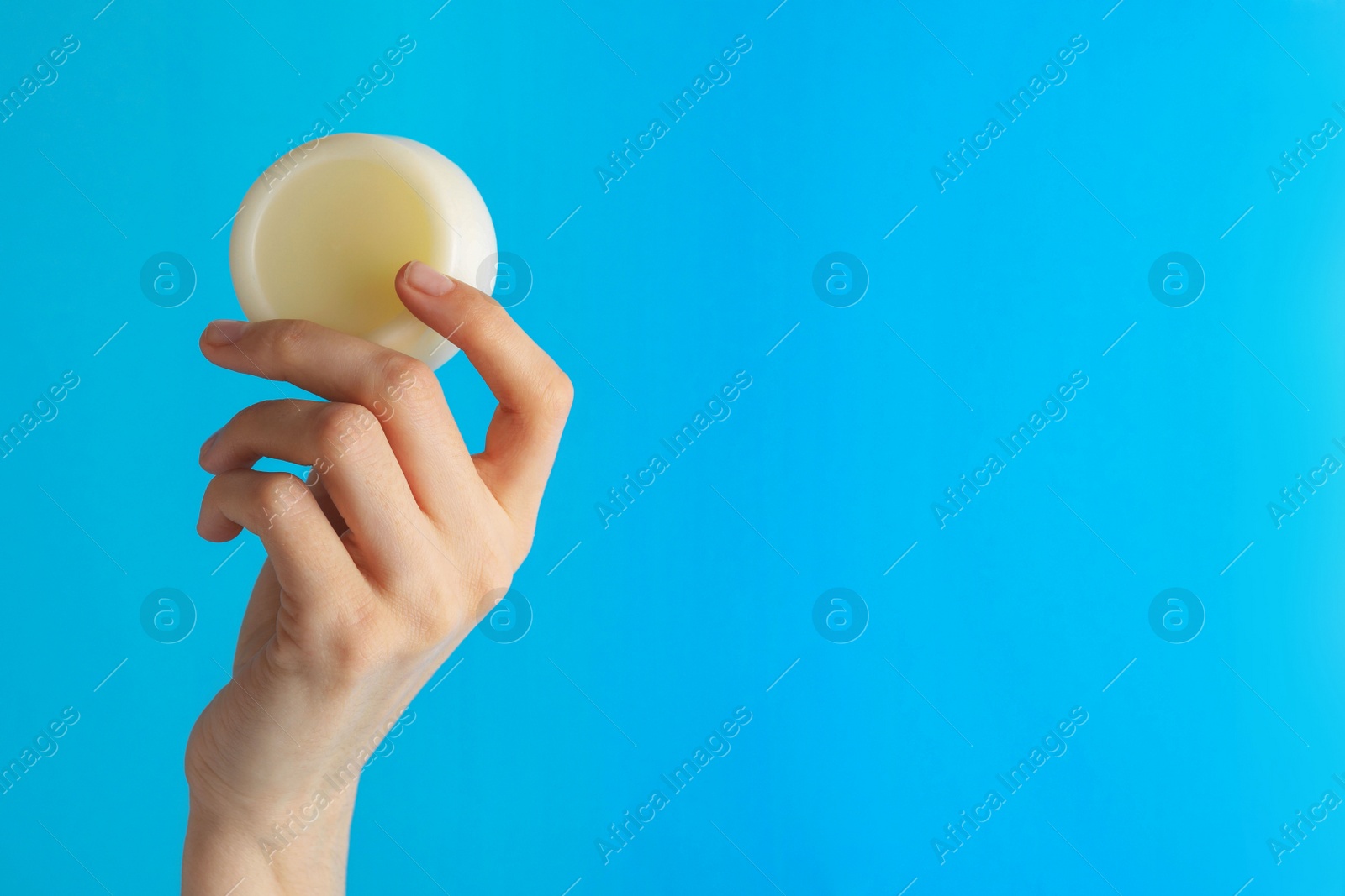 Photo of Woman holding solid shampoo bar against light blue background, closeup. Space for text