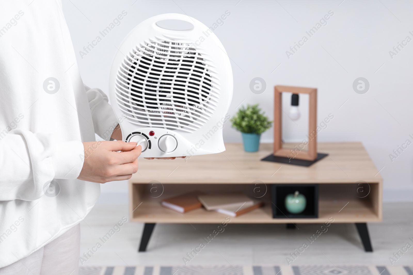 Photo of Woman turning on electric fan heater at home, closeup. Space for text