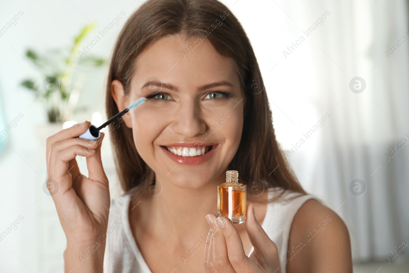Photo of Young woman applying oil on her eyelashes at home