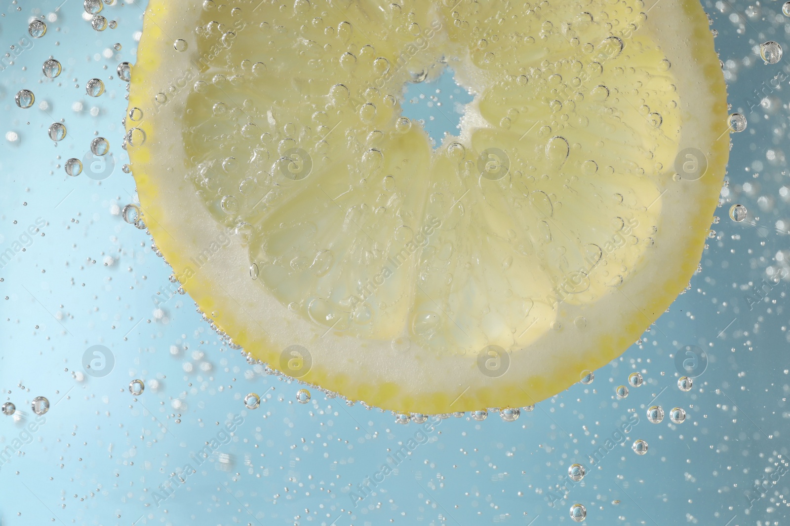 Photo of Juicy lemon slice in soda water against light blue background, closeup