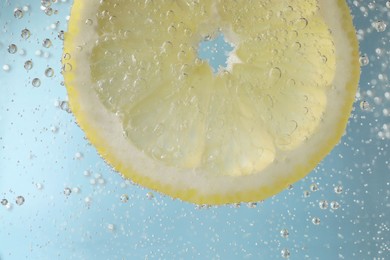 Photo of Juicy lemon slice in soda water against light blue background, closeup