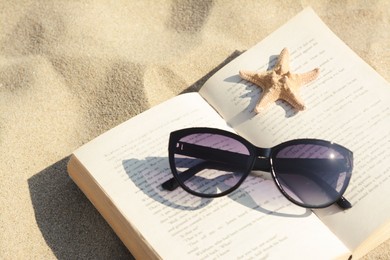 Photo of Beautiful sunglasses, book and starfish on sand, closeup