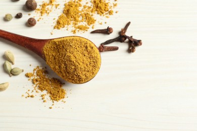 Photo of Spoon with dry curry powder and other spices on light wooden table, above view. Space for text