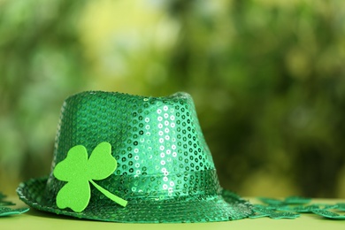 Photo of Green sequin hat with clover leaf on table against blurred background, space for text. St Patrick's Day celebration