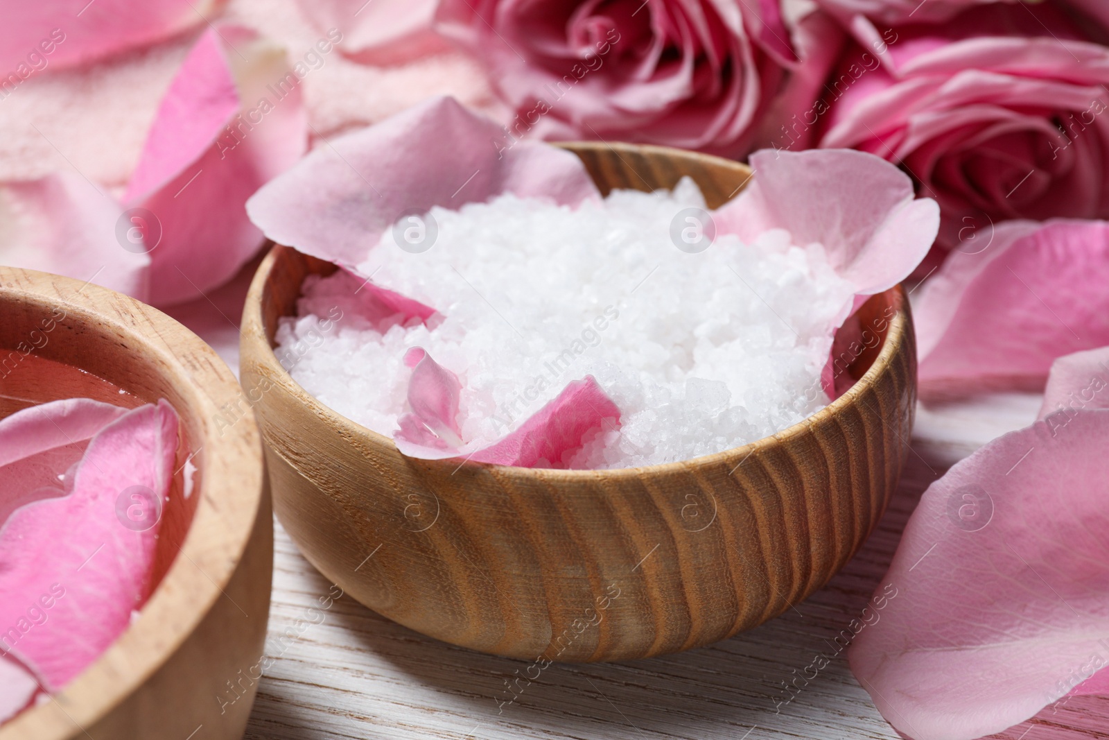 Photo of Bowl with sea salt and beautiful petals of roses on white wooden table, closeup