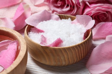 Photo of Bowl with sea salt and beautiful petals of roses on white wooden table, closeup