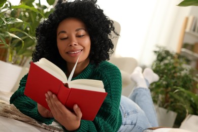 Relaxing atmosphere. Happy woman reading book near potted houseplants at home