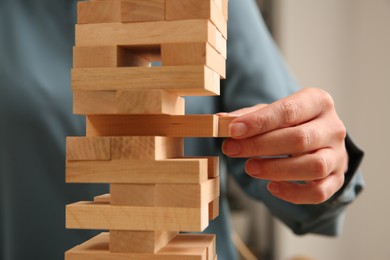 Photo of Playing Jenga. Woman removing wooden block from tower indoors, closeup