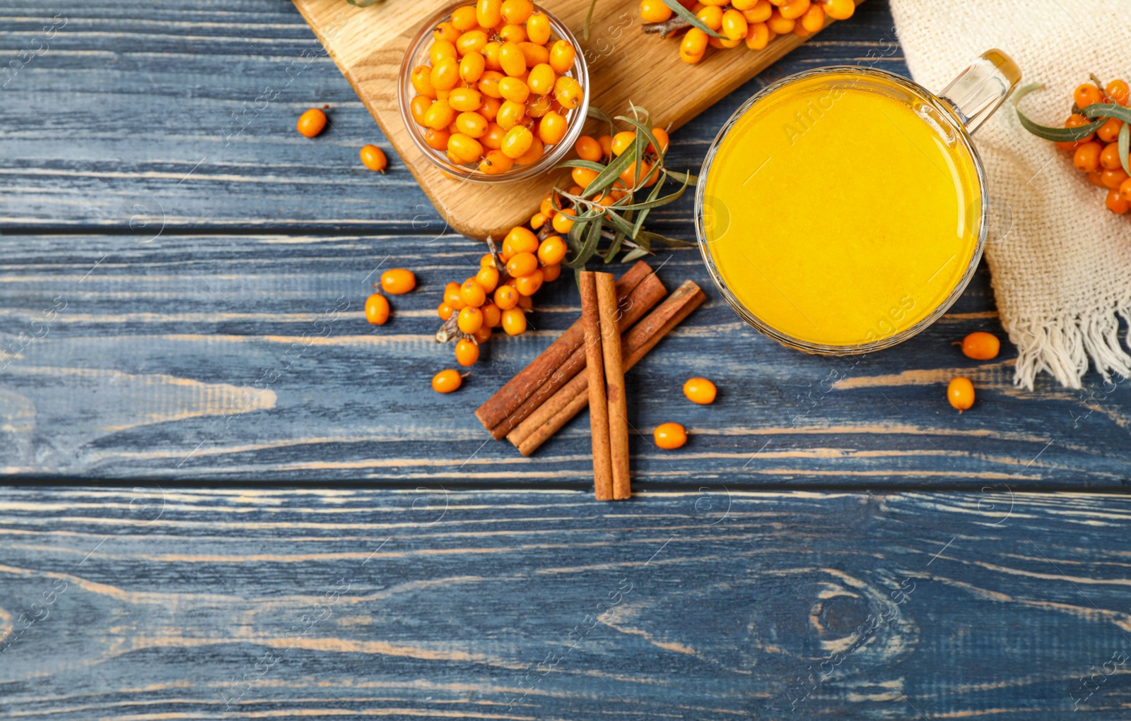 Photo of Sea buckthorn tea and fresh berries on blue wooden table, flat lay. Space for text