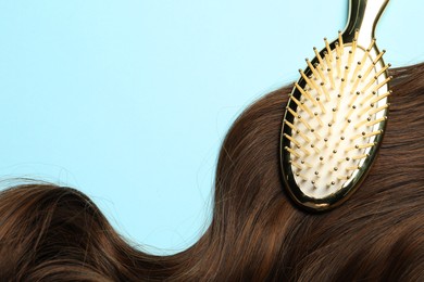 Photo of Stylish brush with brown hair strand on light blue background, top view. Space for text