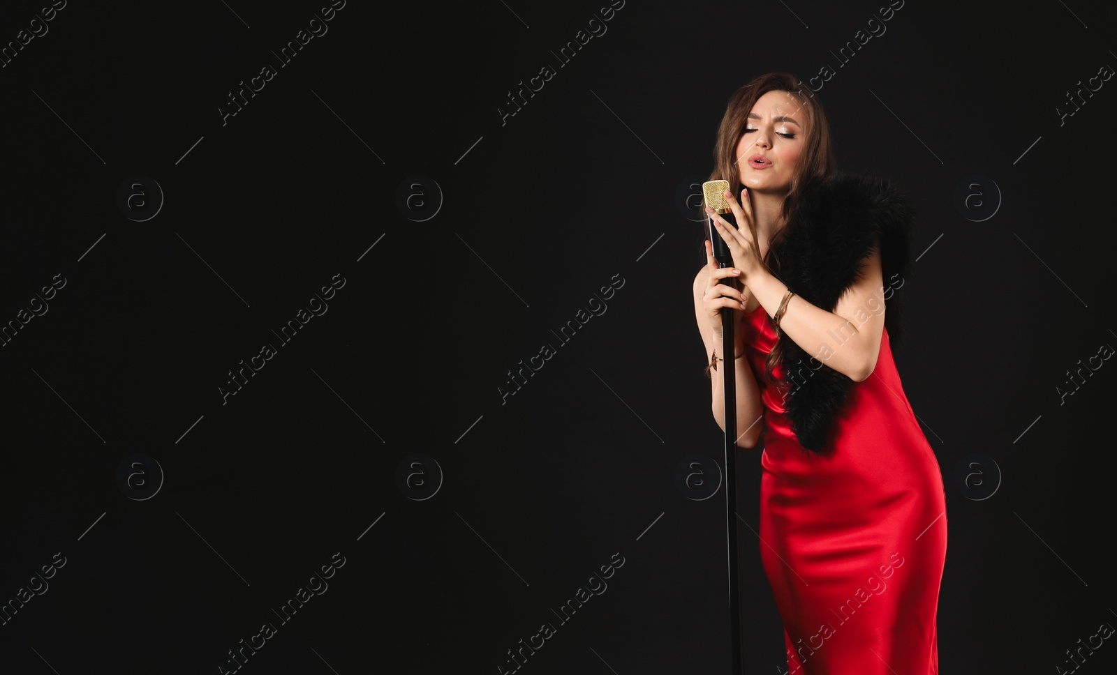 Photo of Beautiful young woman in stylish dress with microphone singing on black background