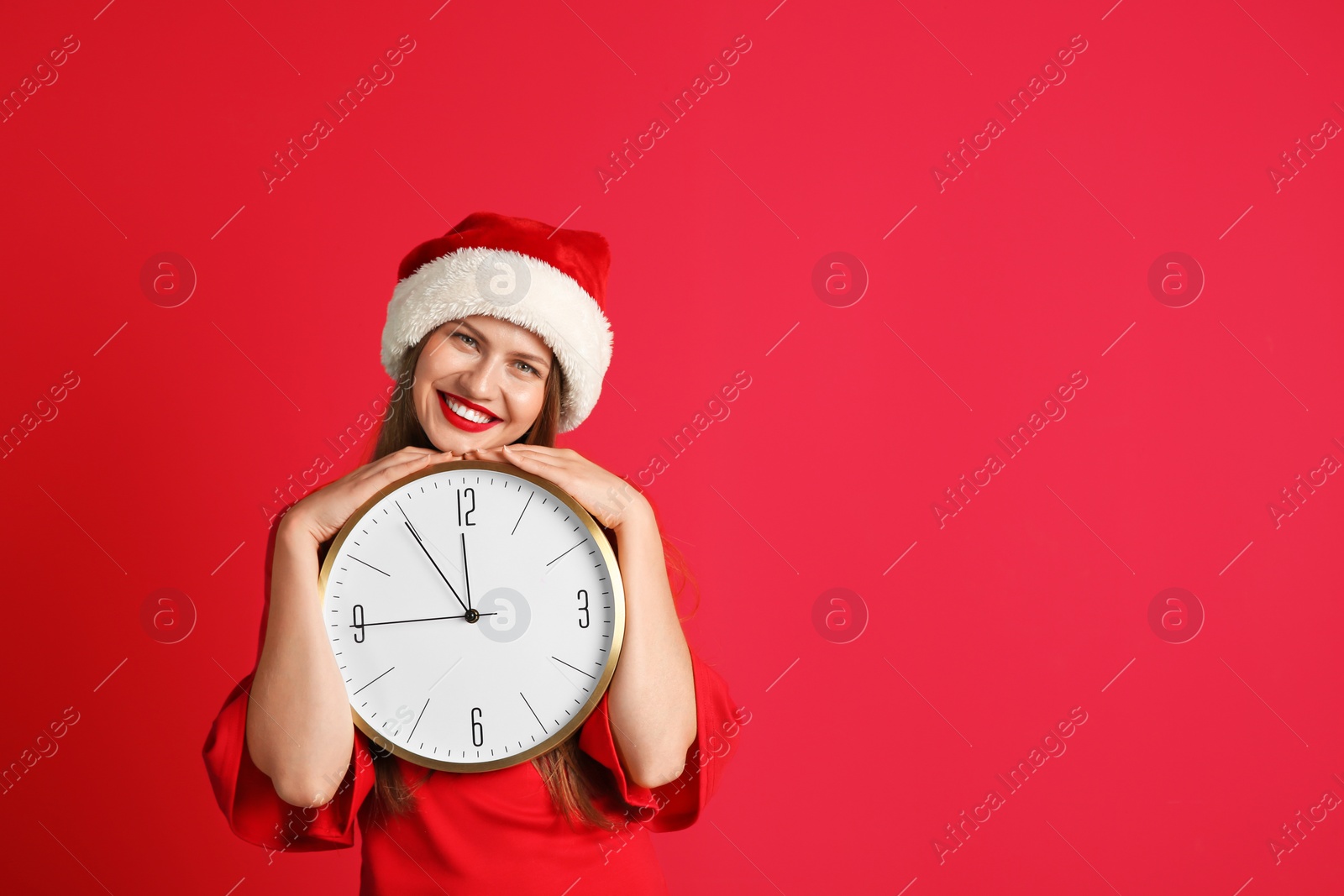 Photo of Young beautiful woman in Santa hat holding big clock on color background. Christmas celebration