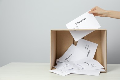 Photo of Woman putting referendum ballot in box on table against light grey background, closeup. Space for text