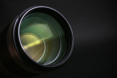 Photo of Modern camera lens on black background, closeup. Space for text
