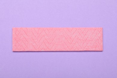 Photo of One stick of tasty chewing gum on violet background, top view