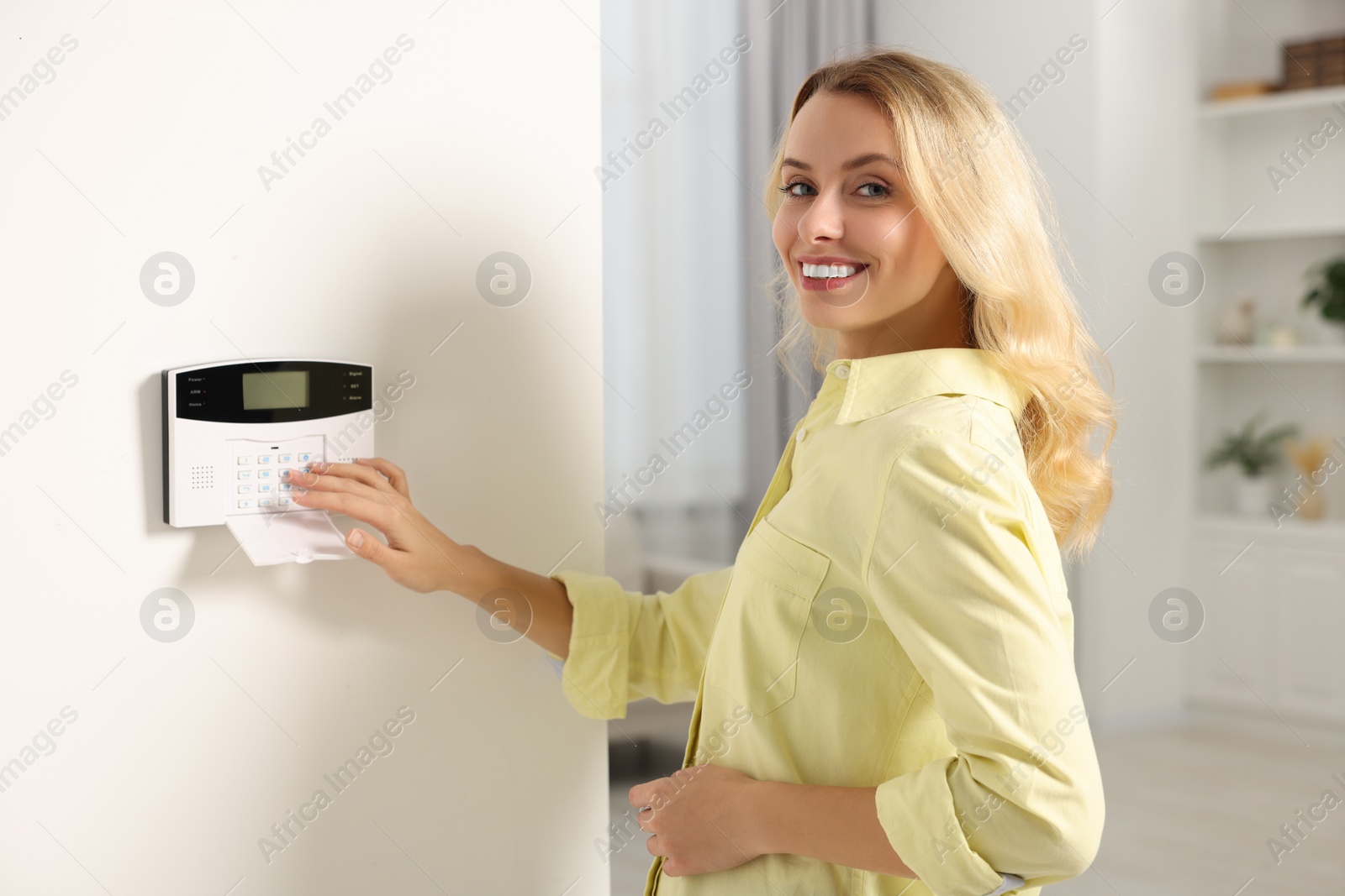 Photo of Smiling woman entering code on home security system in room