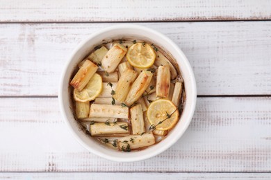 Dish with baked salsify roots, lemon and thyme on white wooden table, top view