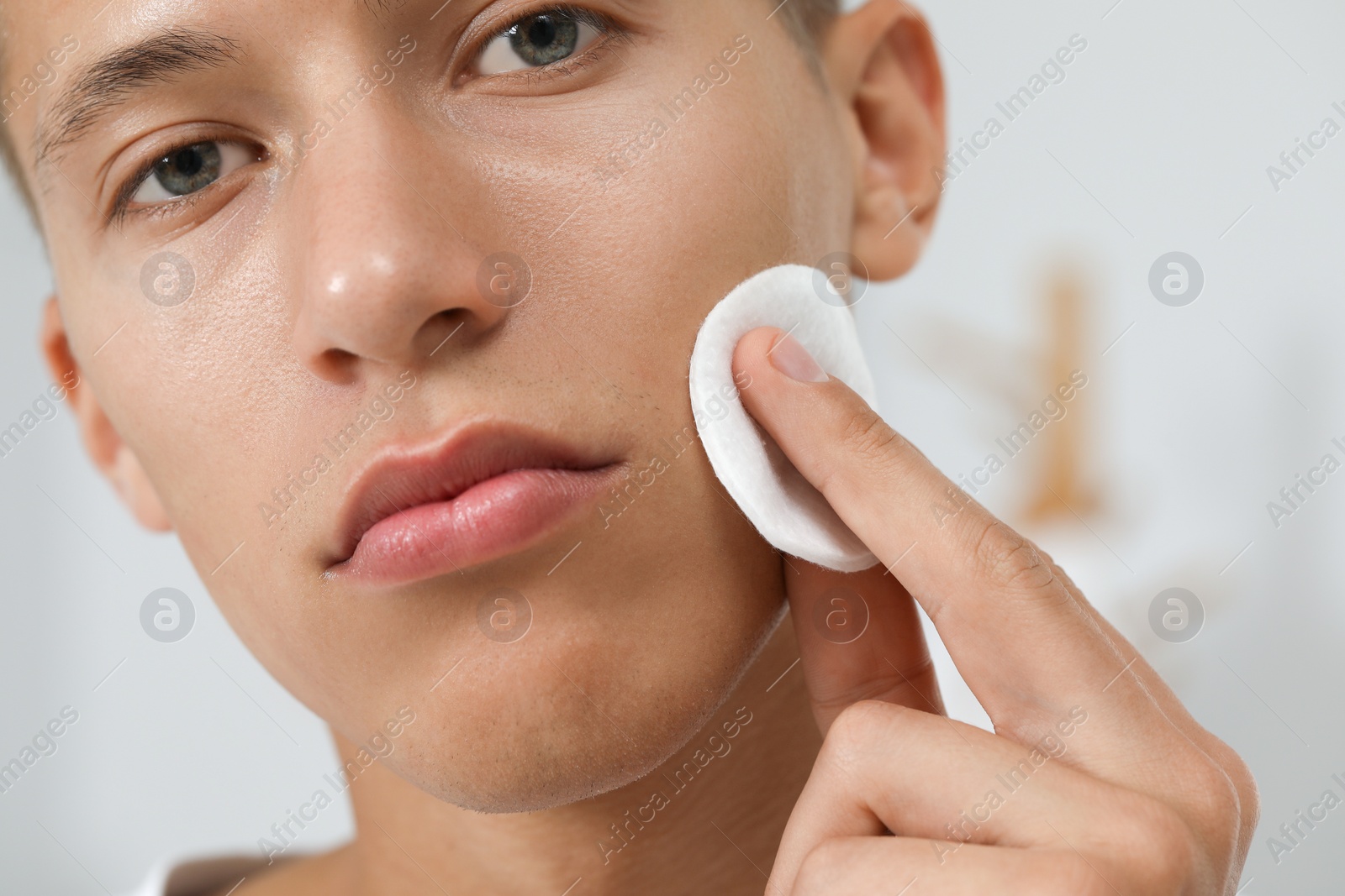 Photo of Handsome man cleaning face with cotton pad against blurred background, closeup