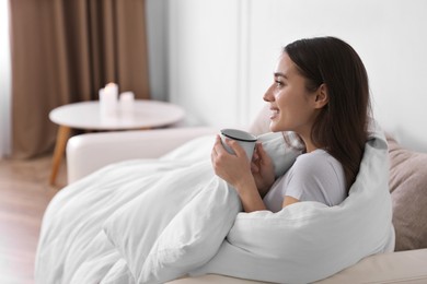 Photo of Woman covered in blanket holding cup of drink on sofa, space for text