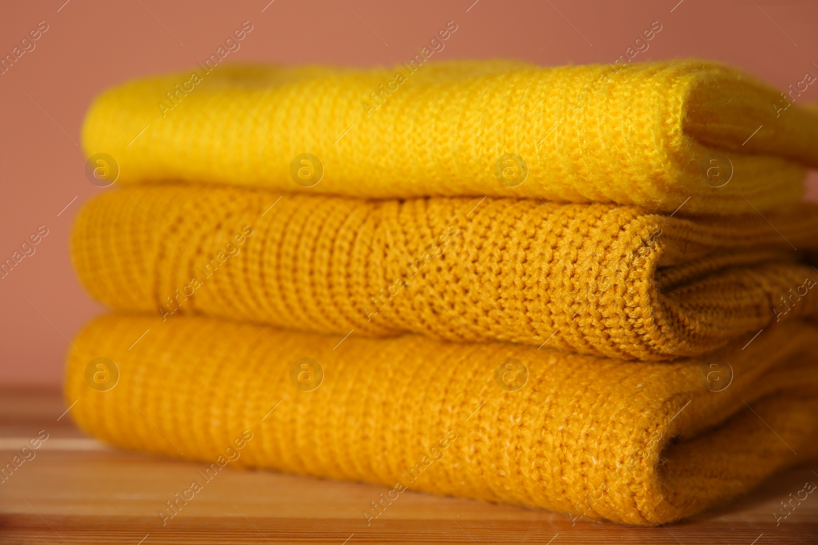 Photo of Stack of folded knitted sweaters on wooden table, closeup