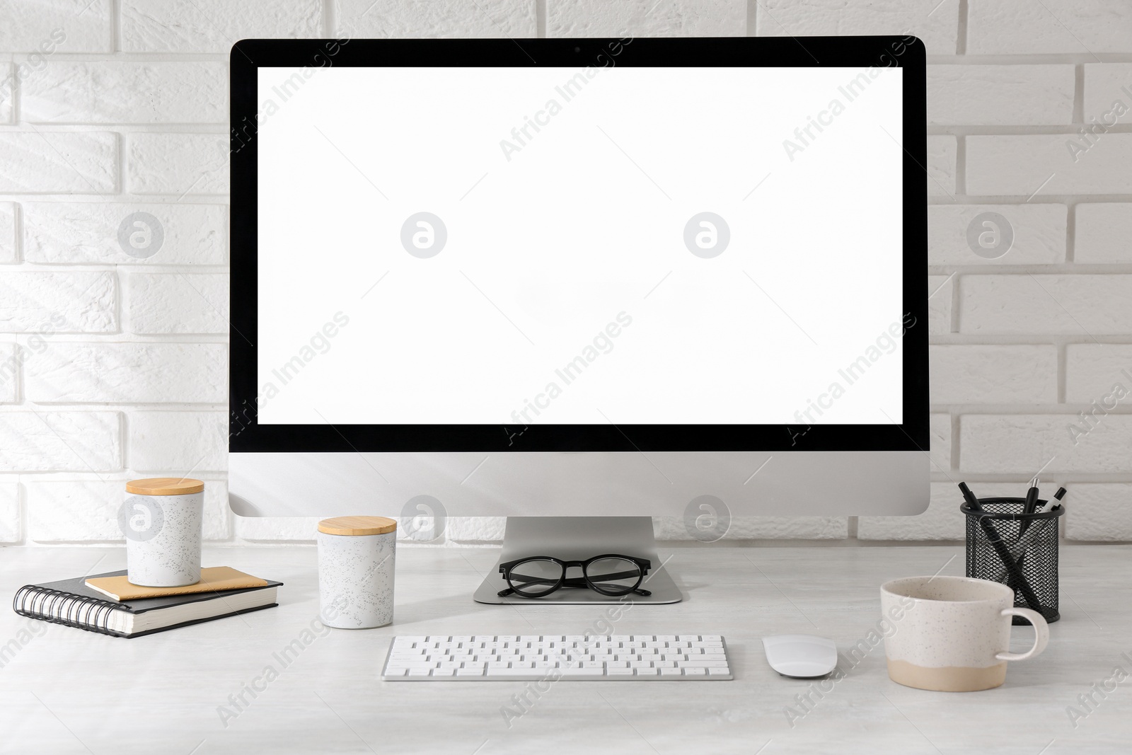 Photo of Office workplace with computer, cup and stationery on light table near white brick wall