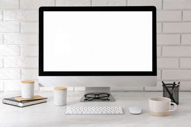 Photo of Office workplace with computer, cup and stationery on light table near white brick wall