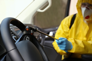 Photo of Person in protective suit disinfecting car, focus on sprayer. Preventive measure during coronavirus pandemic