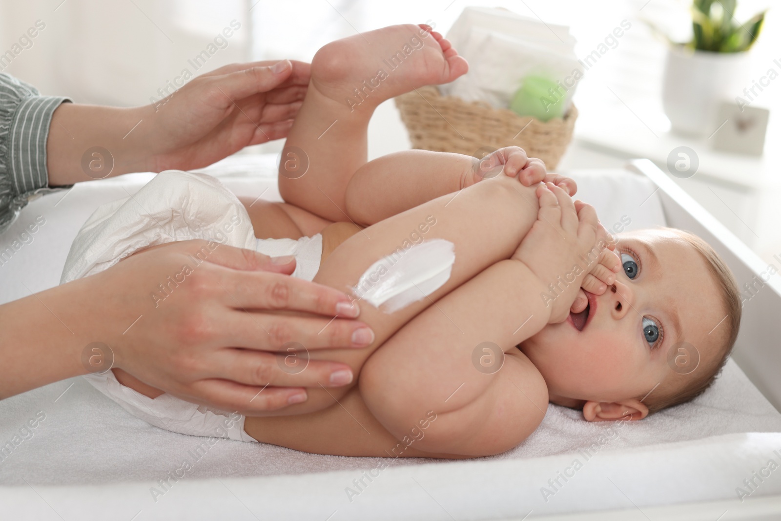 Photo of Mother applying body cream on her little baby at home, closeup