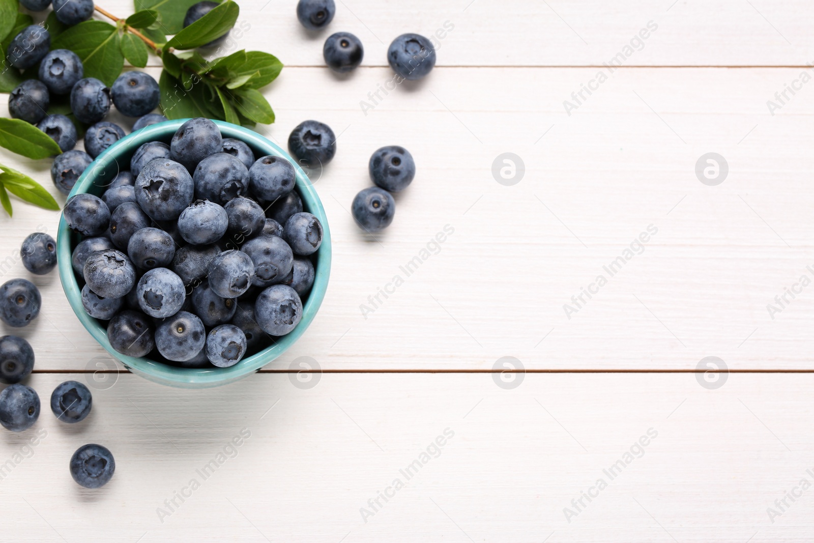 Photo of Tasty fresh blueberries and green leaves on white wooden table, flat lay. Space for text