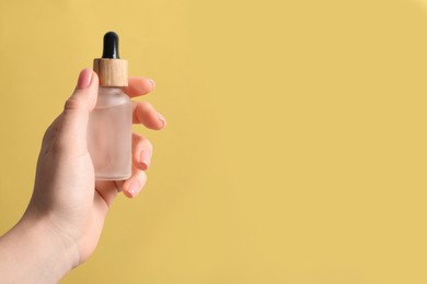 Photo of Woman holding bottle with serum against pale orange background, closeup. Space for text