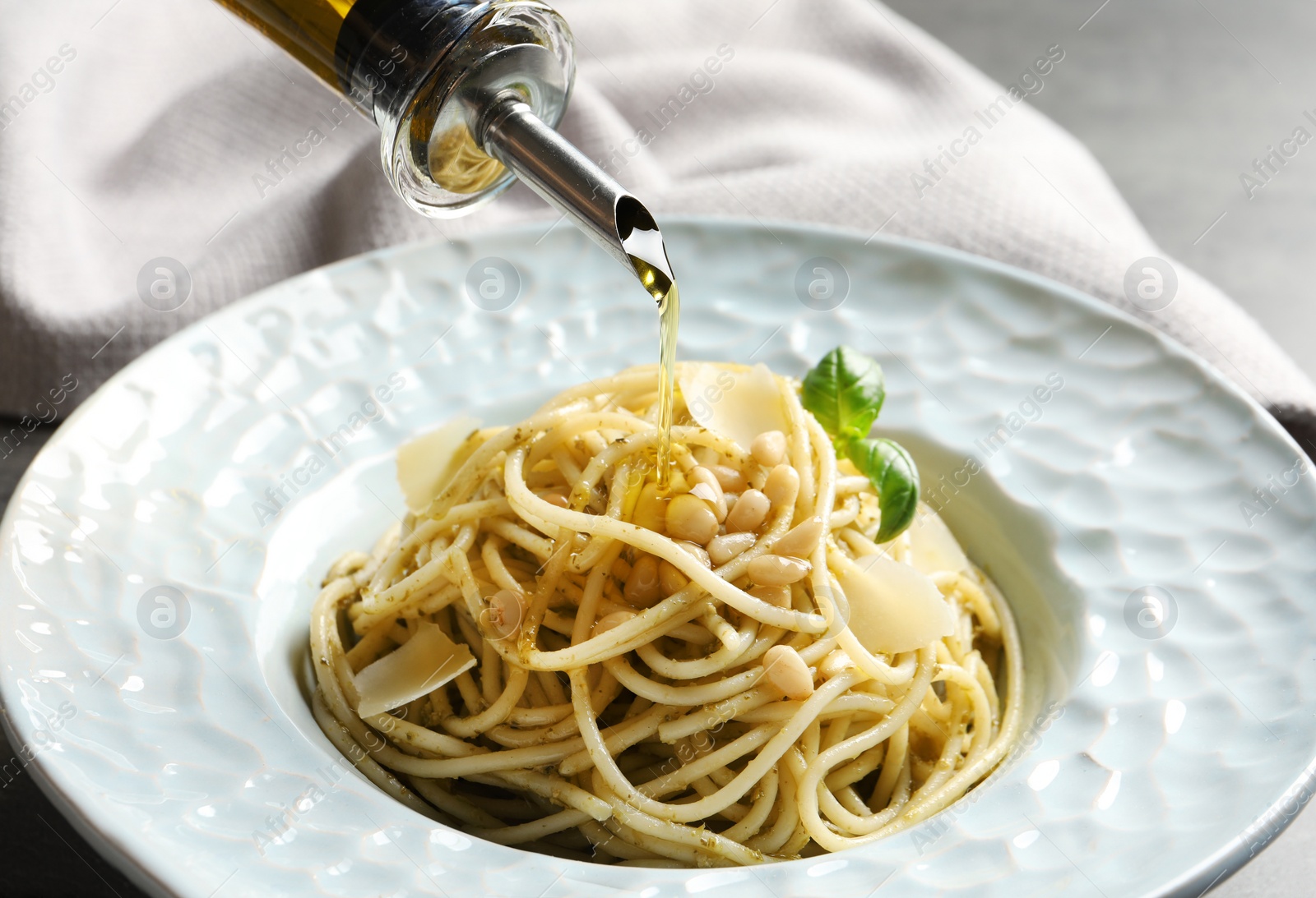 Photo of Dressing delicious basil pesto pasta with olive oil, closeup