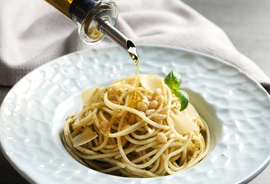 Photo of Dressing delicious basil pesto pasta with olive oil, closeup