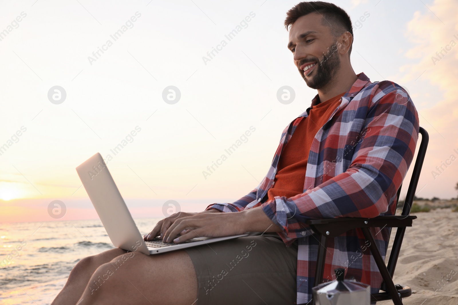 Photo of Man using laptop in camping chair on sandy beach