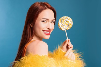 Happy woman with red dyed hair and green lollipop on light blue background