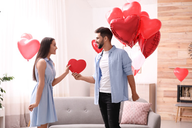 Photo of Lovely couple with heart shaped balloons in living room. Valentine's day celebration