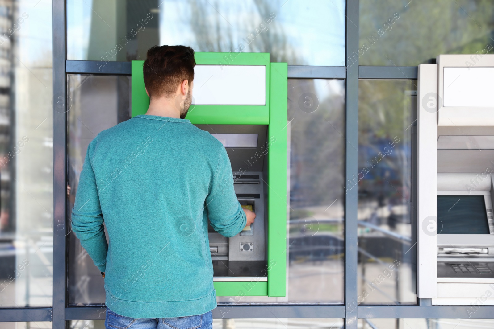 Photo of Young man using modern cash machine outdoors
