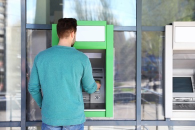 Young man using modern cash machine outdoors