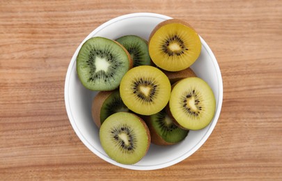 Photo of Bowl of many cut fresh kiwis on wooden table, top view