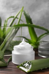Photo of Jar of cosmetic product and cut aloe vera leaves on wooden table