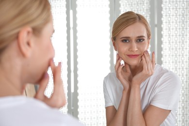 Photo of Happy young woman with clean skin looking at mirror in bathroom