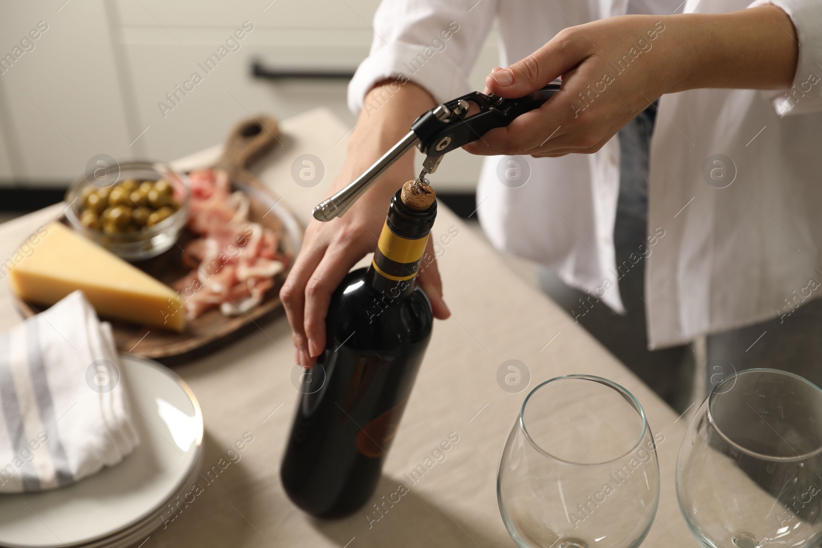 Photo of Woman opening wine bottle with corkscrew at table indoors, closeup