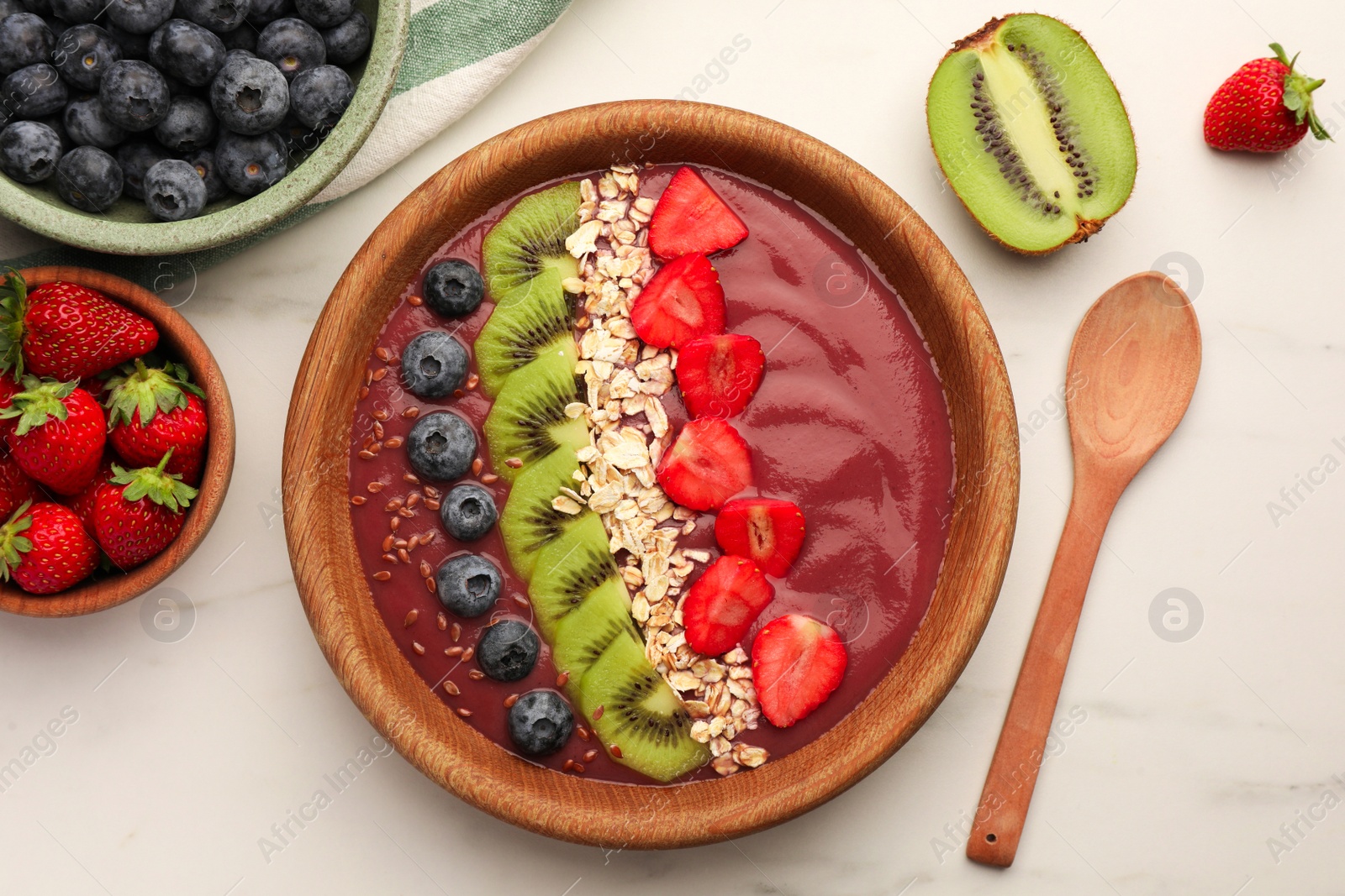 Photo of Bowl of delicious smoothie with fresh blueberries, strawberries, kiwi slices and oatmeal on white marble table, flat lay